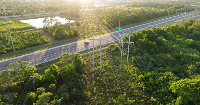Electric power towers support high voltage cables crossing over active highway with cars and trucks. Energy infrastructure over roadway.