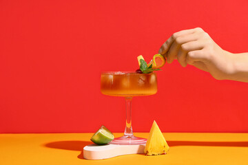 Woman decorating glass of tasty Mai Tai cocktail on colorful background