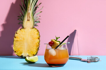Glass of tasty Mai Tai cocktail garnished with cherry and pineapple on blue table against pink...
