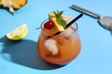 Glass of tasty Mai Tai cocktail garnished with cherry and lime on blue background