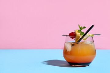 Glass of tasty Mai Tai cocktail garnished with cherry and pineapple on blue table against pink...
