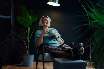 Middle aged woman relaxing with cup of hot drink in scandy style hygge interior home. Cozy...
