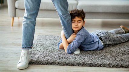 Don't go, dad. Upset boy embracing his father leg, begging daddy to stay with him, lying on the...