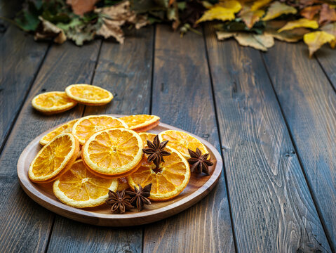 Fall plank table with dried dehydrated orange slices, star anise on brown wood plate with autumn leaves
