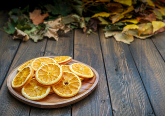 Fall brown wood plank table with dried orange slices on brown wooden plate with autumn leaves