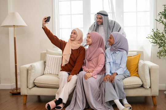 Muslim family wearing hijab video call greeting with relatives on smartphone smiling together at home, digital connection modern communication, arabic family with social platform, islamic content - Powered by Adobe