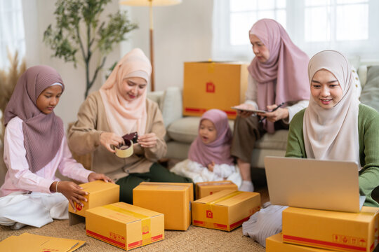 Muslim big family working together on online business packing parcels for shipping using laptop at home, halal brand startup teamwork, delivery, e-commerce with family and SME, muslim entrepreneurship - Powered by Adobe