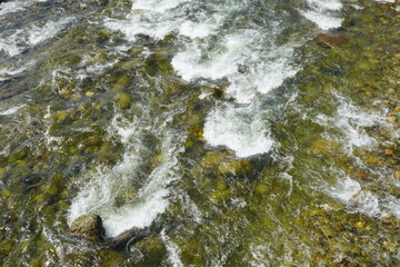 Clear mountain river stream with visible stones under water, dynamic flowing current creating white...