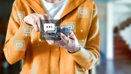A person in a yellow sweater holds a mobile phone, touching the screen to send feedback. Digital...