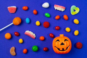 Halloween candy assortment with colorful sweets lollipop jelly beans gummy teeth and pumpkin bucket on vibrant purple background. 