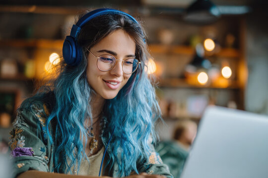 Smiling freelance girl with blue hair working on laptop in loft cafe with modern interior, concept of online work - Powered by Adobe