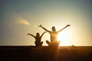 Fototapeta premium joyful parent and child in silhouette during a golden hour sunset, their arms raised in an expressive outdoor setting symbolizing togetherness, happiness, and family future hope 