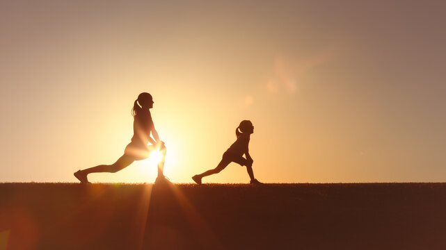 Parent child stretching exercises on a hilltop during sunset, creating a serene silhouette effect, emphasizing fitness, relaxation, and the beauty of nature