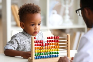 Little African curly boy playing with colorful abacus in psychologist's office. Concept of child development and helping children with mental disorder