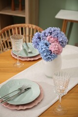 Stylish setting with plates and vase of flowers on wooden table in dining room. Interior design