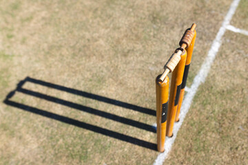 Three cricket stumps with bails standing on grassy pitch next to chalk line