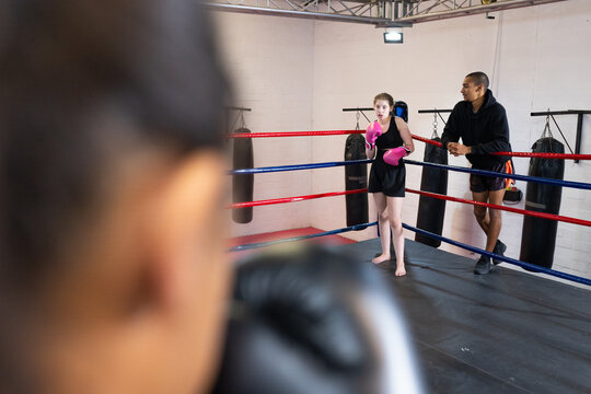 Teenage female boxer with male trainer practicing in boxing ring with pink gloves and punching bags - Powered by Adobe