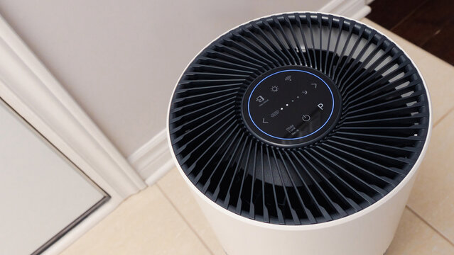 Close up view of Air Purifier with Black Fan. Black Round Electronic Device with Buttons and Bright Lights on White Background