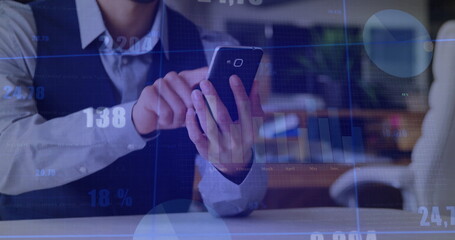 Tapping business professional analyzing data on smartphone at office desk, with charts overlay