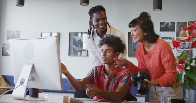 Pointing creative team reviewing designs on desktop monitor in studio, with DSLR camera and plant - Powered by Adobe