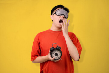 man waking up tired holding alarm clock against yellow background