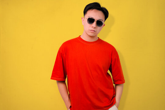 confident young man wearing sunglasses standing against yellow and orange background - Powered by Adobe