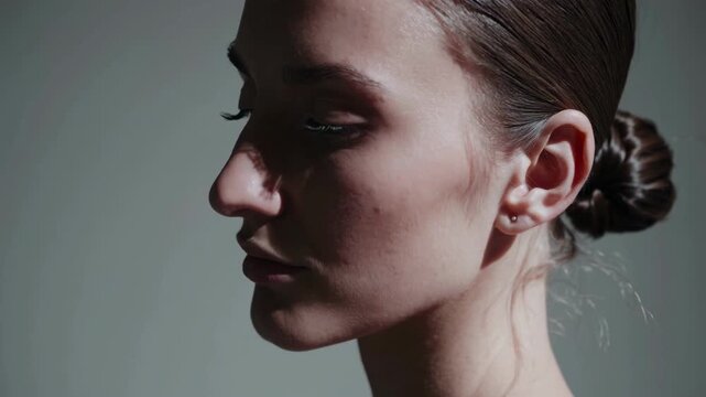Profile view of a woman with a sleek bun, captured in soft lighting. The video style emphasizes elegance and subtlety from a side angle.