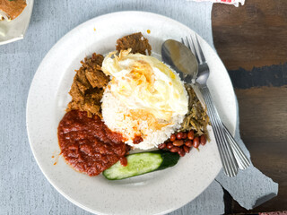 Nasi Lemak with fried egg, beef rendang, sambal, anchovies, peanuts, and cucumber.