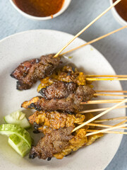 Close up view of satay (sate), a popular Malaysian street food.  Served together with peanut sauce, sliced cucumber, onion and rice cube (nasi impit)
