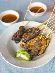 Close up view of satay (sate), a popular Malaysian street food.  Served together with peanut sauce, sliced cucumber, onion and rice cube (nasi impit)