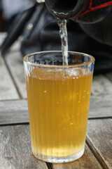 Close-up of iced tea being poured from a pitcher into a glass on a wooden table, capturing a refreshing moment in a casual outdoor setting.