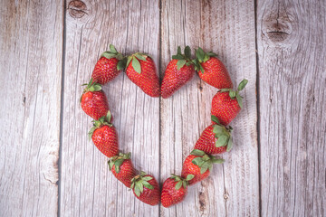 Fresh ripe strawberries arranged in the shape of a heart on a rustic wooden background. Concept of love, healthy eating, organic food, natural lifestyle, summer fruit, and nutrition.