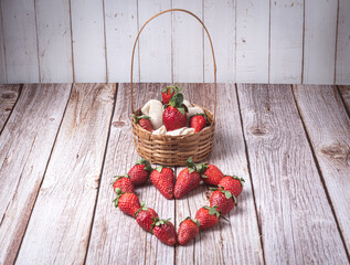 Wicker basket filled with fresh ripe strawberries on a rustic wooden table with a linen cloth in...