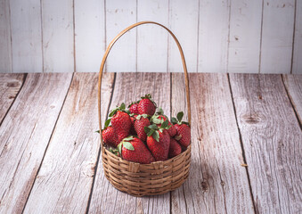 Wicker basket filled with fresh ripe strawberries on a rustic wooden table with a linen cloth in...