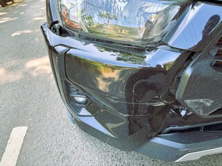 A close-up view shows the black car's damaged and dented bumper on the front due to a traffic...