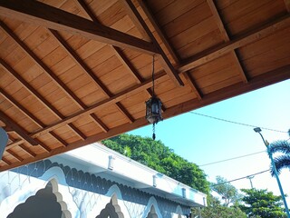 A calming tropical scene featuring a traditional wooden roof and an antique pendant light. Lush...