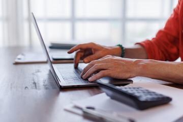 Fototapeta premium Business man Using laptop computer and working at office with calculator document on desk, doing planning analyzing the financial report, business plan investment, finance analysis concept. 