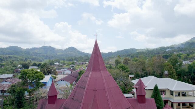 Aerial drone footage of a red roof church in Ruteng, Flores, Indonesia. The video captures the church architecture with a cross on top, set against a scenic mountain landscape and village houses.
