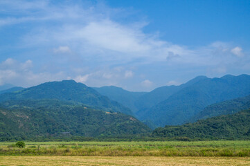 Obraz premium Scenic Mountain Range Under Blue Sky: A landscape featuring a series of mountains receding into the distance under a blue sky with some clouds.