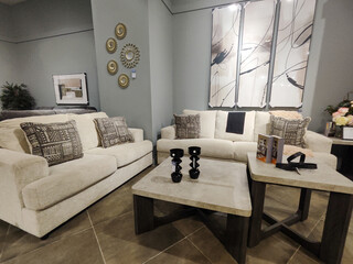 A tastefully decorated living room showroom with two light-colored sofas, textured throw pillows,...