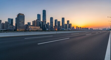 Fototapeta premium An empty highway stretches towards a modern city skyline at sunset, featuring towering skyscrapers and a vibrant sky blending orange and blue hues. Urban architecture and infrastructure.