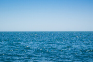 Naklejka premium Minimalist ocean horizon with deep blue water under a clear sky. Calm rippling waves with sparkling highlights create abundant copy space for design. 