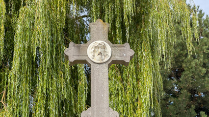 A stone cross with the face of Jesus in a cemetery