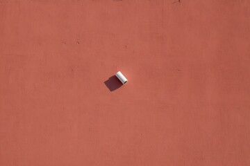 A small white cylinder rests on a red surface, casting a shadow