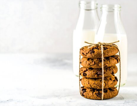 Stacked chocolate chip cookies tied with twine, beside milk bottles