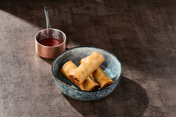Fried duck spring rolls, rustic lighting, overhead composition in ceramic bowl with copper saucepot