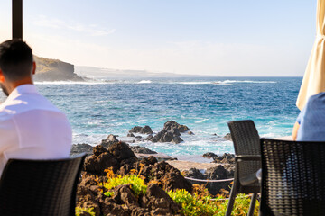 Tourists enjoy sea and mountain views along the volcanic coastline from an outdoor seaside cafe restaurant at Garachico, Spain, on the Canary Island of Tenerife.