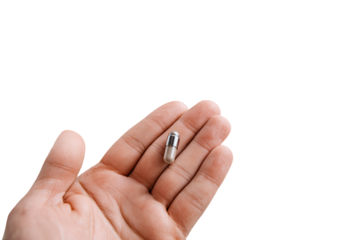A single, light gray pill capsule held in a person's open hand against a black background