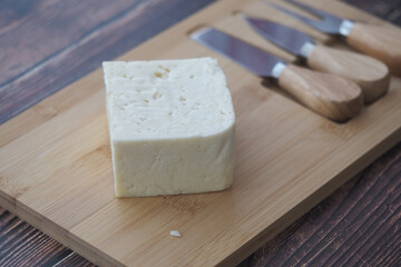 Fresh cheese on a wooden cutting board with knives