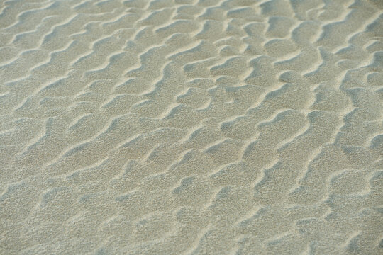Close-up of rippled sand dunes, showing texture and natural patterns. Uneven sand texture, beach background, top down view. Closeup shot of sand texture on the beach as background.